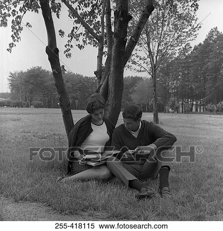 Stock Photography - Young couple sitting under tree and reading book. Fotosearch