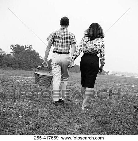 Stock Photo - Young couple with picnic basket, walking in field. Fotosearch