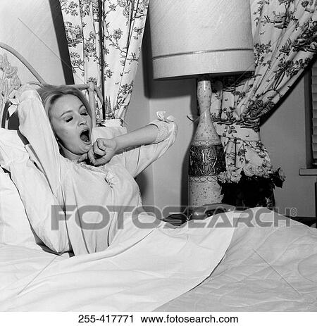 Stock Image - Young woman in bed yawning. Fotosearch