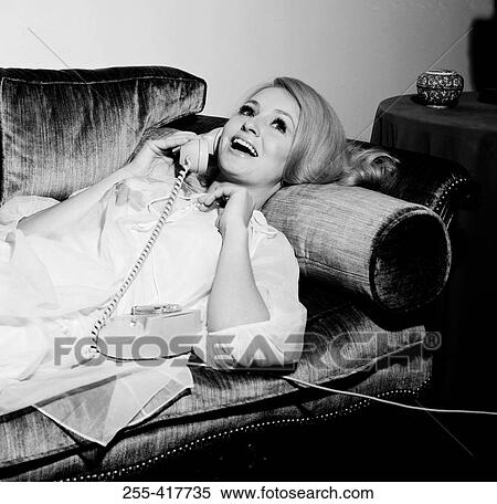 Stock Photography - Young woman laying on sofa, using telephone. Fotosearch