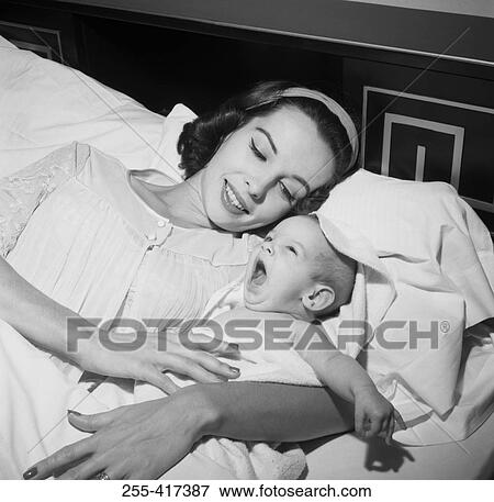 Stock Photo - Young woman lying in bed with her baby. Fotosearch