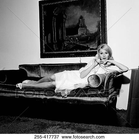 Stock Photo - Young woman reclining on sofa, using telephone. Fotosearch