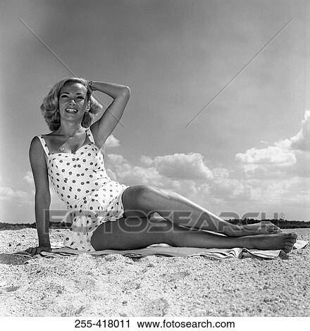 Stock Image - Young woman wearing swimsuit sitting on beach. Fotosearch