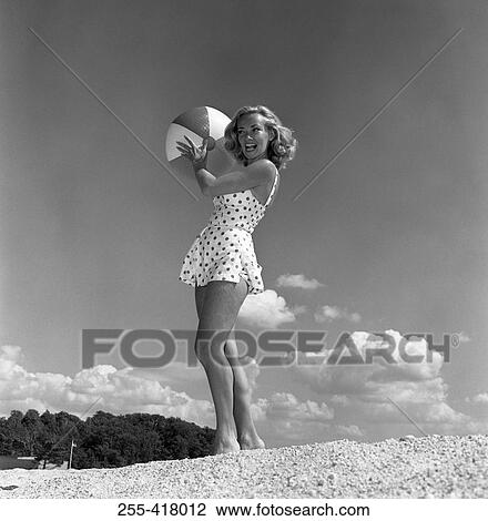 Stock Image - Young woman wearing swimsuit standing on beach and holding beach ball. Fotosearch