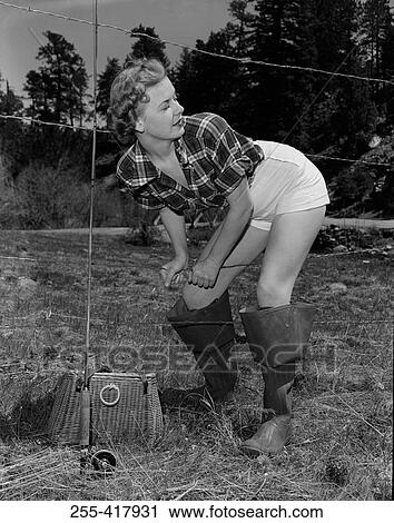 Stock Image - Young woman with fishing rod and basket crossing barbed wire fence. Fotosearch