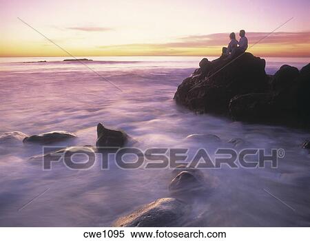 Couple Sitting On Rocks At Sunset Over Wave Painted Shores Of Laguna Beach California Stock Photography Cwe1095 Fotosearch