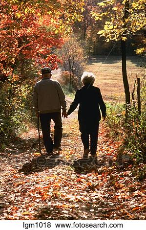 Senior couple holding hands and walking along dirt road lined with fall