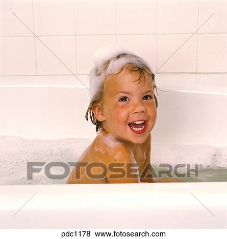 A Smiling Little Girl Taking A Bubble Bath With Shampoo In Her Hair And Hands In The Tub Stock Photo