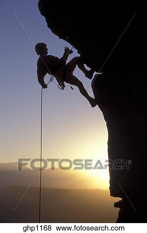 Silhouette Of A Mountain Climber Rappelling Down A Cliff Stock