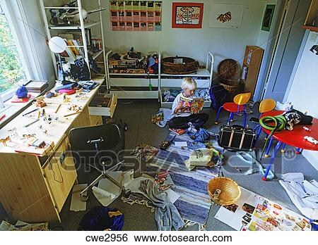 Young Boy In Bedroom Amid Messy Sea Of Toys Stock Photograph