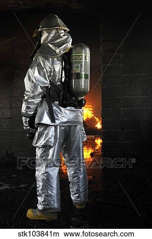 Picture - A firefighter waits for a fire to get bigger before attempting to extinguish the flames.. Fotosearch