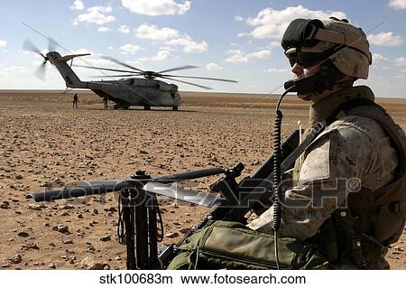 Picture - A Marine assembles a radio antenna as a CH-53E Super Stallion helicopter lands nearby.. Fotosearch