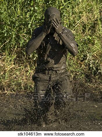 A participant wipes mud from his face after jumping in a pond. View Large Photo Image Picture - A participant wipes mud from his face after jumping in a pond.. Fotosearch