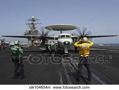 A plane director guides an E-2C Hawkeye onto the catapult for launch. View Large Photo Image Picture - A plane director guides an E-2C Hawkeye onto the catapult for launch.. Fotosearch