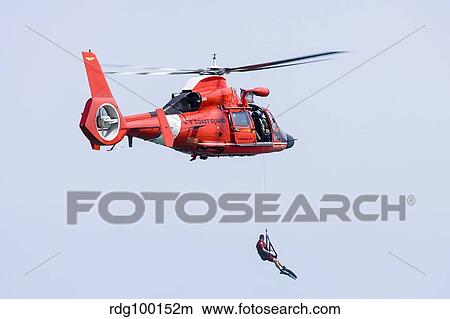 A rescue swimmer is lowered from a U. S. Coast Guard HH-65 Dolphin helicopter. View Large Photo Image Picture - A rescue swimmer is lowered from a U. S. Coast Guard HH-65 Dolphin helicopter.. Fotosearch