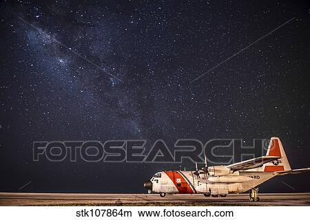 Picture - A U. S. Coast Guard C-130 Hercules parked on the tarmac on a starry night.. Fotosearch