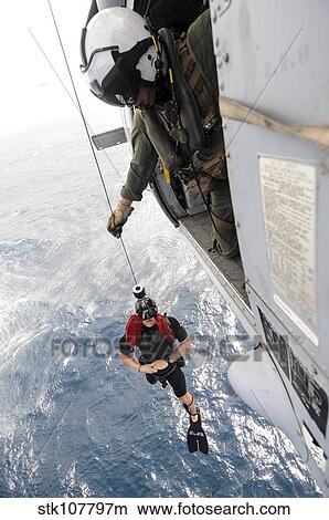 Picture - Aircrewman assists in hoisting a member into an MH-60S Sea Hawk.. Fotosearch