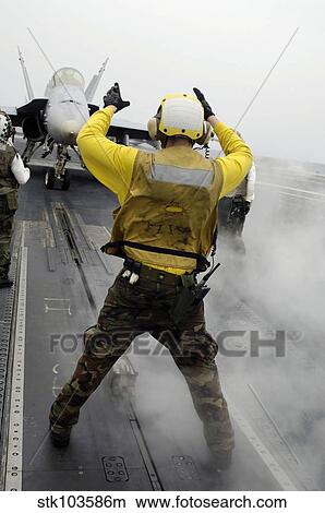 An aircraft director signals a F/A-18C Hornet on the flight deck of USS Kitty Hawk. View Large Photo Image Picture - An aircraft director signals a F/A-18C Hornet on the flight deck of USS Kitty Hawk.. Fotosearch
