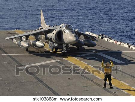 Picture - An Airman directs an AV-8B Harrier jet aircraft on the flight deck of USS Essex.. Fotosearch