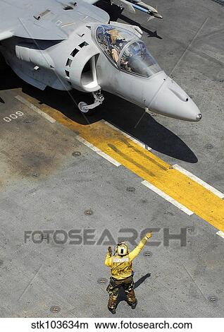 An Airman uses hand signals to direct an AV-8B Harrier during flight operations aboard USS Peleliu. View Large Photo Image Picture - An Airman uses hand signals to direct an AV-8B Harrier during flight operations aboard USS Peleliu.. Fotosearch