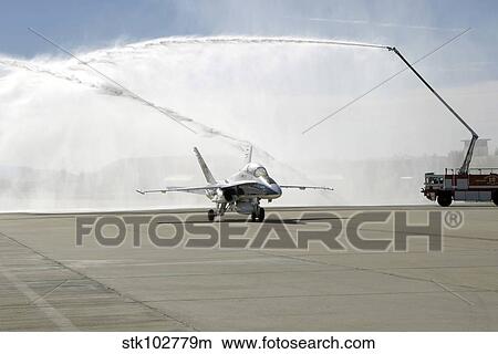 Picture - An F-18 aircraft taxies beneath the spray from fire trucks.. Fotosearch