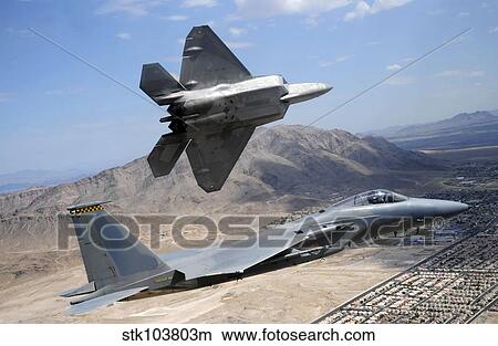 An F-22 Raptor aircraft turns away while an F-15 Eagle flies the approach over Nevada. View Large Photo Image Picture - An F-22 Raptor aircraft turns away while an F-15 Eagle flies the approach over Nevada.. Fotosearch