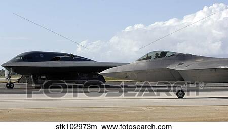 Picture - An F-22 Raptor taxis while a B-2 Spirit waits for clearance.. Fotosearch