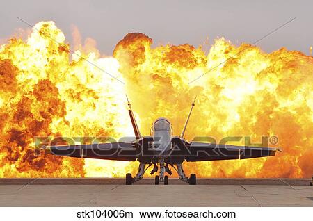 An F/A-18 Hornet sits on the flight line as a wall of fire detonates behind it. View Large Photo Image Picture - An F/A-18 Hornet sits on the flight line as a wall of fire detonates behind it.. Fotosearch