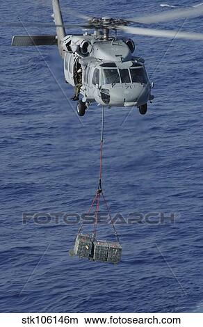 An MH-60S Knighthawk transports supplies during a replenishment at sea. View Large Photo Image Picture - An MH-60S Knighthawk transports supplies during a replenishment at sea.. Fotosearch