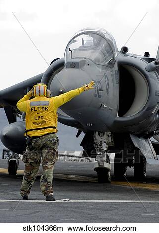 Aviation Boatswain's Mate directs the pilot of an AV-8B Harrier II. View Large Photo Image Picture - Aviation Boatswain's Mate directs the pilot of an AV-8B Harrier II.. Fotosearch