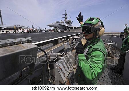 Aviation Boatswain's Mate signals to a shooter as an F/A-18E Super Hornet prepares to launch. View Large Photo Image Picture - Aviation Boatswain's Mate signals to a shooter as an F/A-18E Super Hornet prepares to launch.. Fotosearch