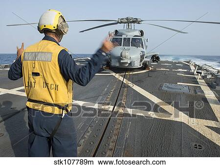 Boatswain's Mate signals to the pilot of an MH-60R Sea Hawk. View Large Photo Image Picture - Boatswain's Mate signals to the pilot of an MH-60R Sea Hawk.. Fotosearch