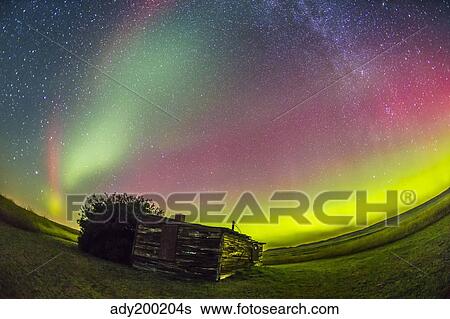 Stock Photograph - Fish-eye lens view of the northern lights above an old ranch in Canada.. Fotosearch