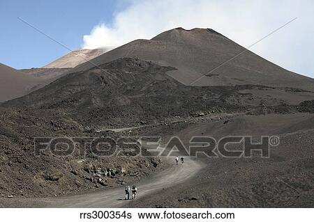 Stock Photograph - Hikers walking towards summit area of Mount Etna volcano, Sicily, Italy.. Fotosearch