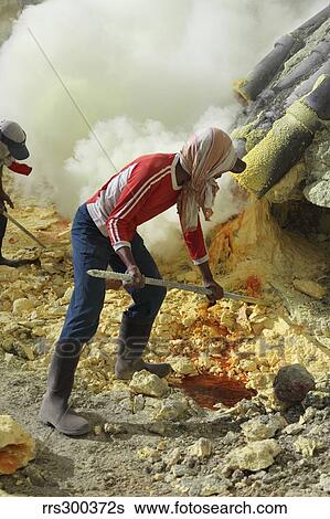 Stock Photograph - Miner breaking up sulphur deposits at Kawah Ijen Volcano, Java, Indonesia.. Fotosearch