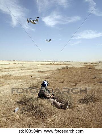 Picture - MV-22B Ospreys fly over U. S. Navy Hospital Corpsman as he acts as an injured pilot waiting to be rescued.. Fotosearch