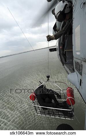 Naval Air Crewman hoists a rescue basket into an MH-60S Sea Hawk helicopter. View Large Photo Image Picture - Naval Air Crewman hoists a rescue basket into an MH-60S Sea Hawk helicopter.. Fotosearch