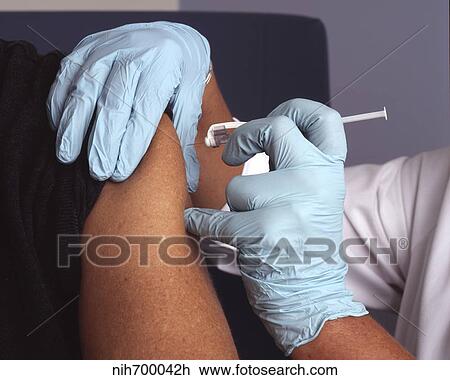 Stock Image - Nurse administers a vaccine into a patient's arm.. Fotosearch
