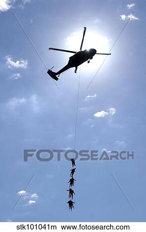 Picture - oldiers and Airmen hang 100 feet above the ground from a UH-60 Blackhawk.. Fotosearch
