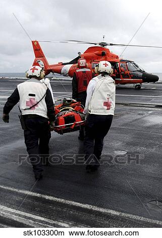 Personnel carry an injured sailor to a coast guard MH-65 Dolphin helicopter. View Large Photo Image Picture - Personnel carry an injured sailor to a coast guard MH-65 Dolphin helicopter.. Fotosearch