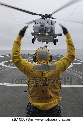Petty Officer guides an SH-60R Sea Hawk helicopter onto the flight deck of USS McClusky. View Large Photo Image Picture - Petty Officer guides an SH-60R Sea Hawk helicopter onto the flight deck of USS McClusky.. Fotosearch