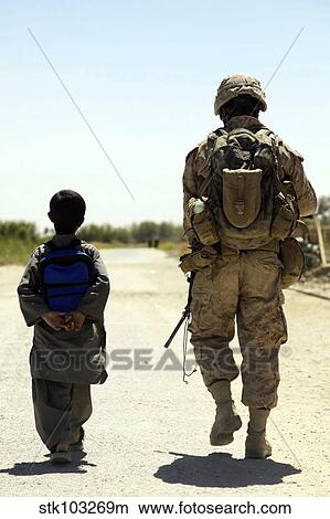 Picture - Rear view of U. S. Marine walking through Nawa bazaar with an Afghan boy in Afghanistan.. Fotosearch