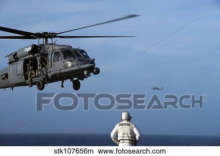 Sailor watches an Air Force HH-60G Pave Hawk helicopter prepare to land. View Large Photo Image Picture - Sailor watches an Air Force HH-60G Pave Hawk helicopter prepare to land.. Fotosearch