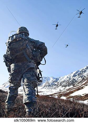 Soldier patrols through Alaska's Chugach Range as UH-60 Black Hawk helicopters fly above. View Large Photo Image Picture - Soldier patrols through Alaska's Chugach Range as UH-60 Black Hawk helicopters fly above.. Fotosearch