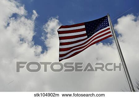 The American Flag blowing in the breeze against a cloudy sky. View Large Photo Image Picture - The American Flag blowing in the breeze against a cloudy sky.. Fotosearch