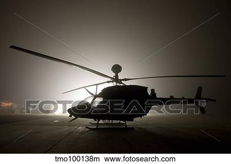 Picture - The illumination from the bright light silhouettes a OH-58D Kiowa helicopter during thick fog.. Fotosearch