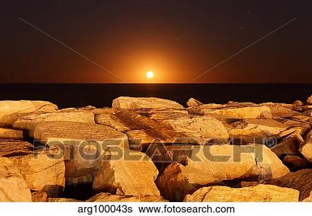 The moon rising behind rocks lit by a nearby fire in Miramar, Argentina. View Large Photo Image Stock Photograph - The moon rising behind rocks lit by a nearby fire in Miramar, Argentina.. Fotosearch