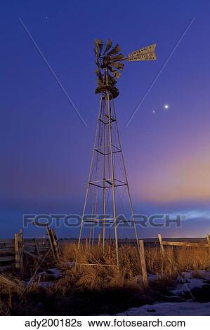 Stock Photograph - Venus and Jupiter are visible behind an old farm water pump windmill, Alberta, Canada.. Fotosearch