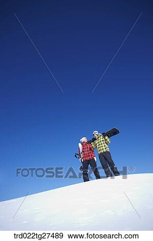 Stock Photo - couple standing on the snow hill with a snow board. Fotosearch