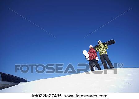 Stock Photography - couple standing on the snow hill with a snow board. Fotosearch